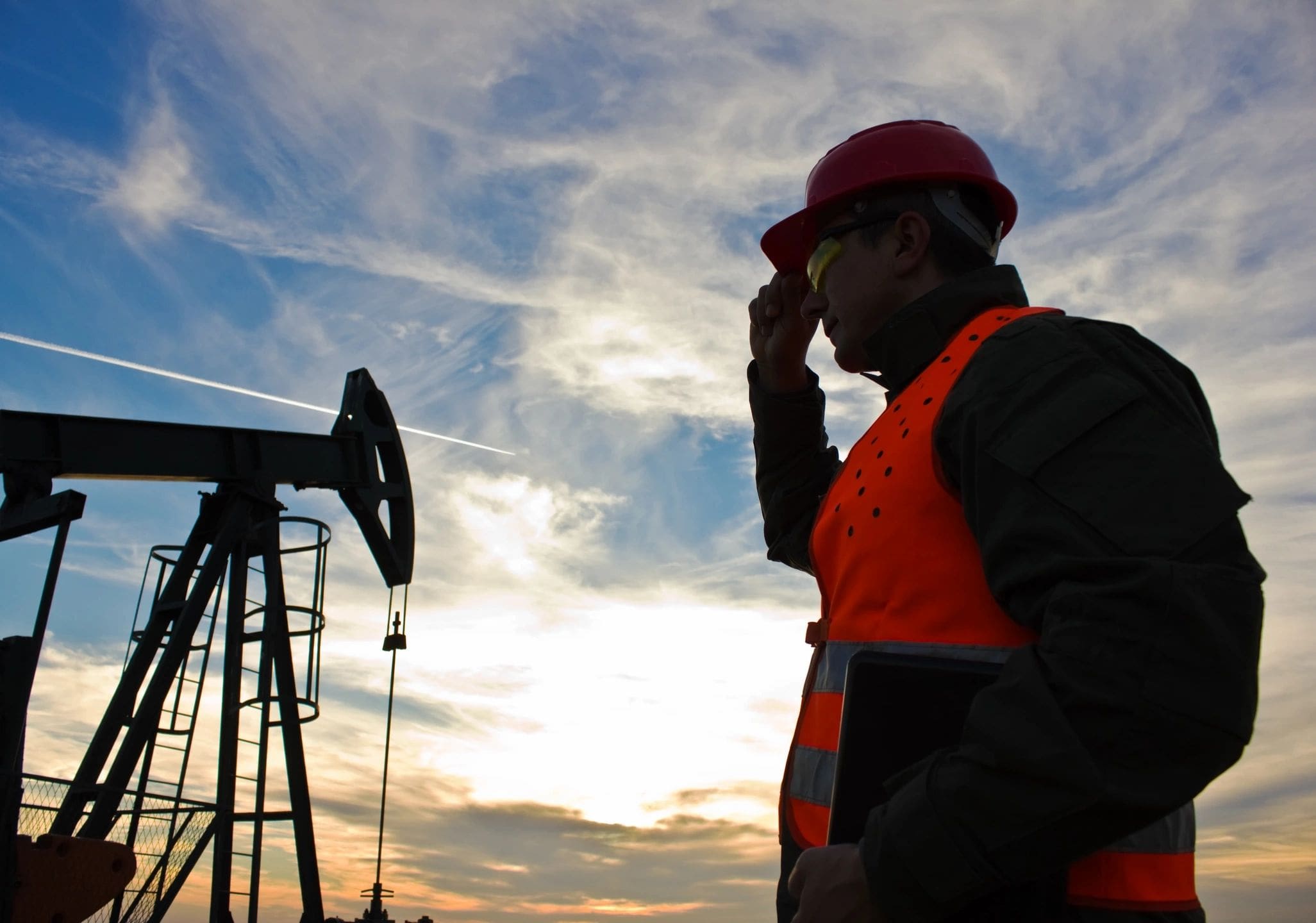 A man in an orange vest standing next to a pump jack.