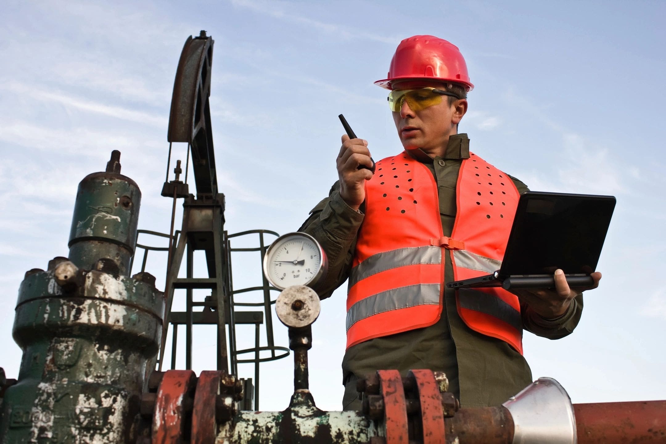 A man in an orange vest and hard hat holding a laptop.